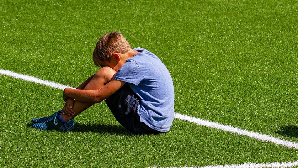 A sad child sitting at the edge of a sports field.