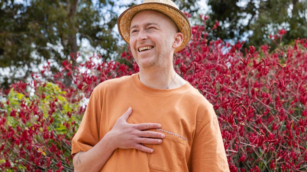 Author Joe Cranbourne standing outside in front of a flowering red bush.