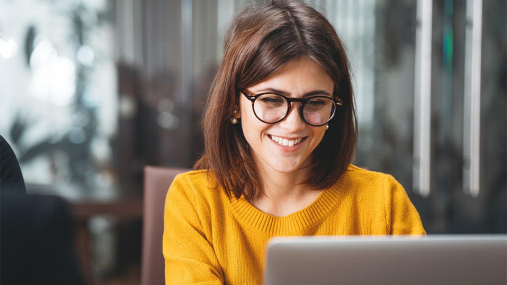 Student in yellow jumper and glasses studying on laptop.
