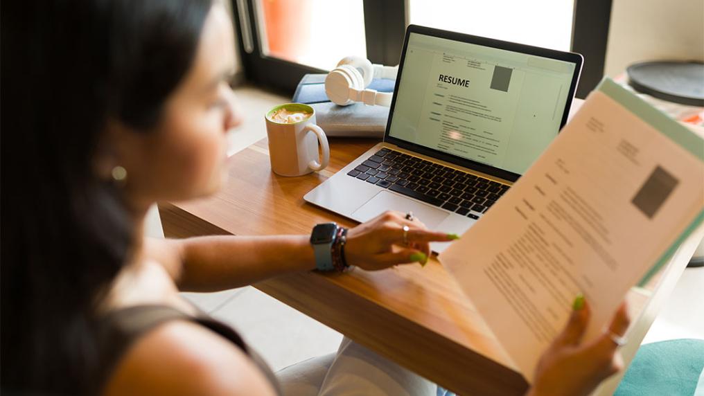 Female student works on their resume on laptop, using a hard copy handout.