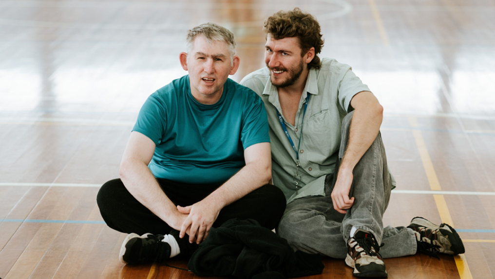 Two students at VU Aspect St Albans. The students are sitting on the gymnasium floor and smiling at the camera.