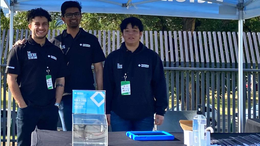 3 young men in uniforms at an info stand with VU branding
