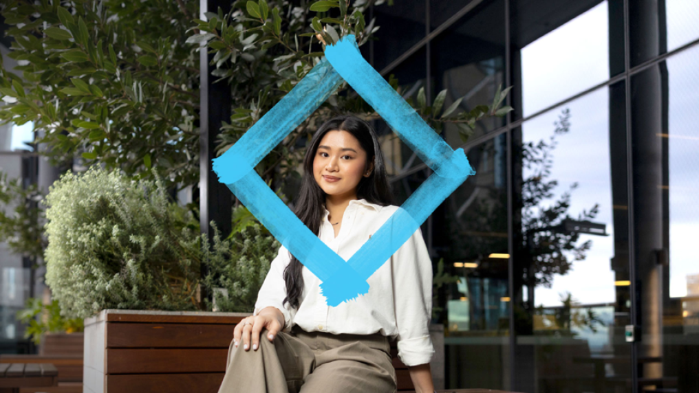 Smiling student sits in VU City Tower balcony area, with the VU blue branded diamond floating in front of them.