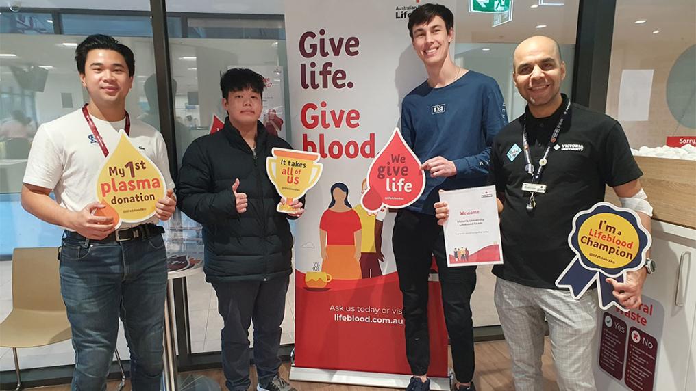 Four VU representatives stand holding signs at the blood donation clinic.