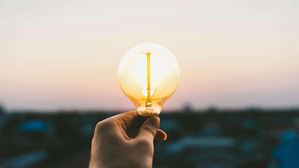 A hand holding a lightbulb held over a city.