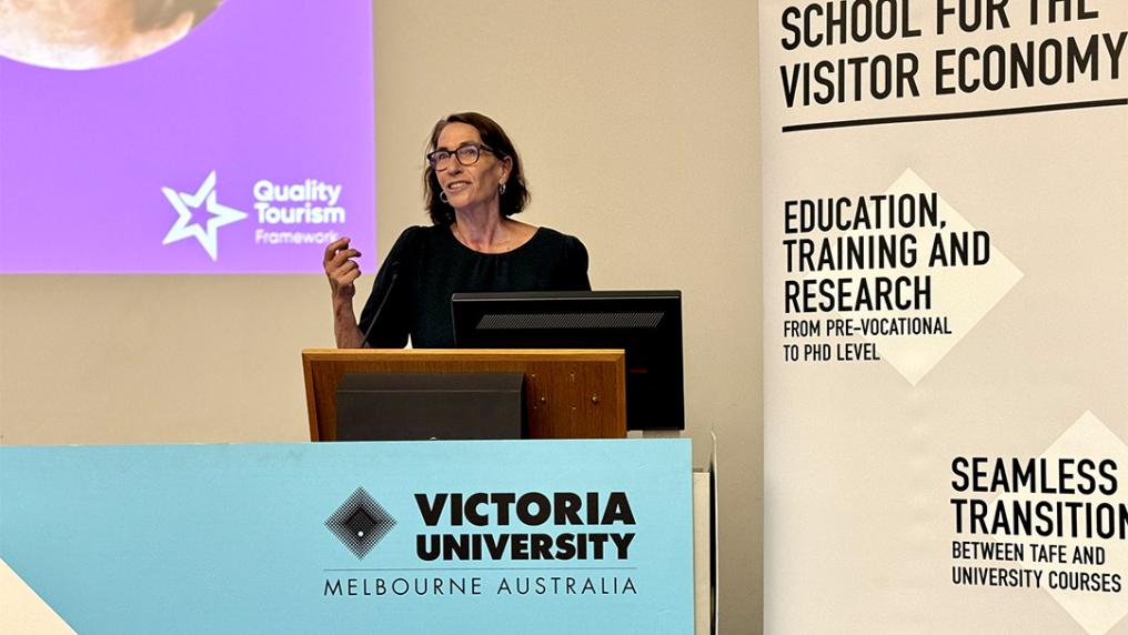 A woman presenting on a podium with Victoria University and School for the Visitor Economy signage
