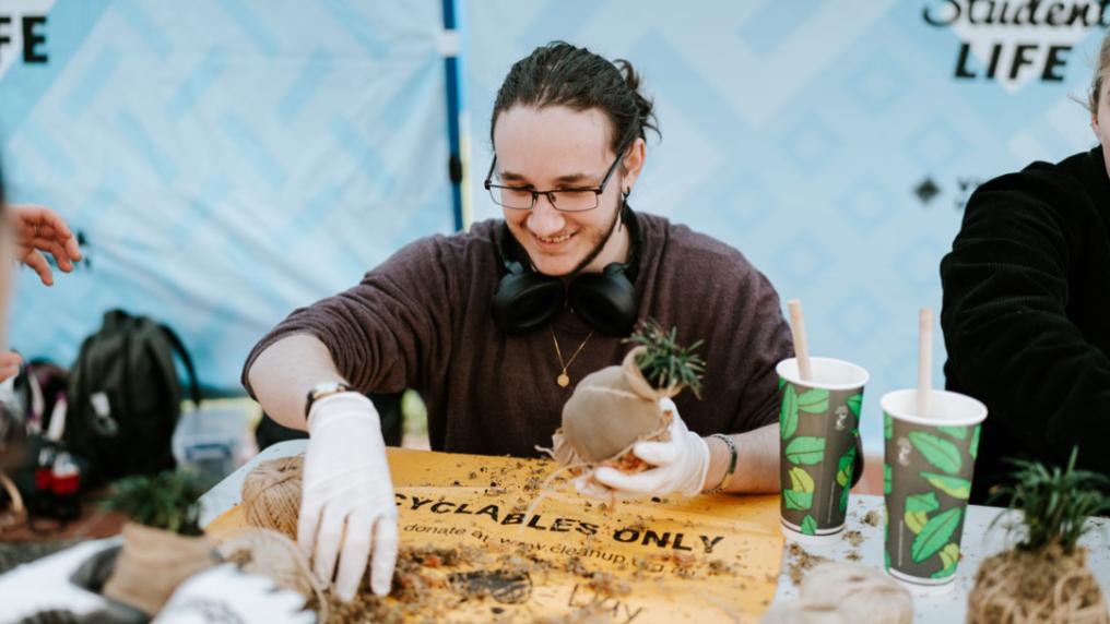 A student holding a small plant pot in one hand while grabbing dirt with their other hand.