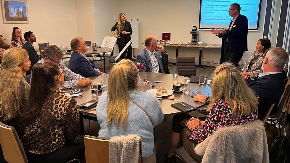 A full room with particpants at round tables, watch in a presentation