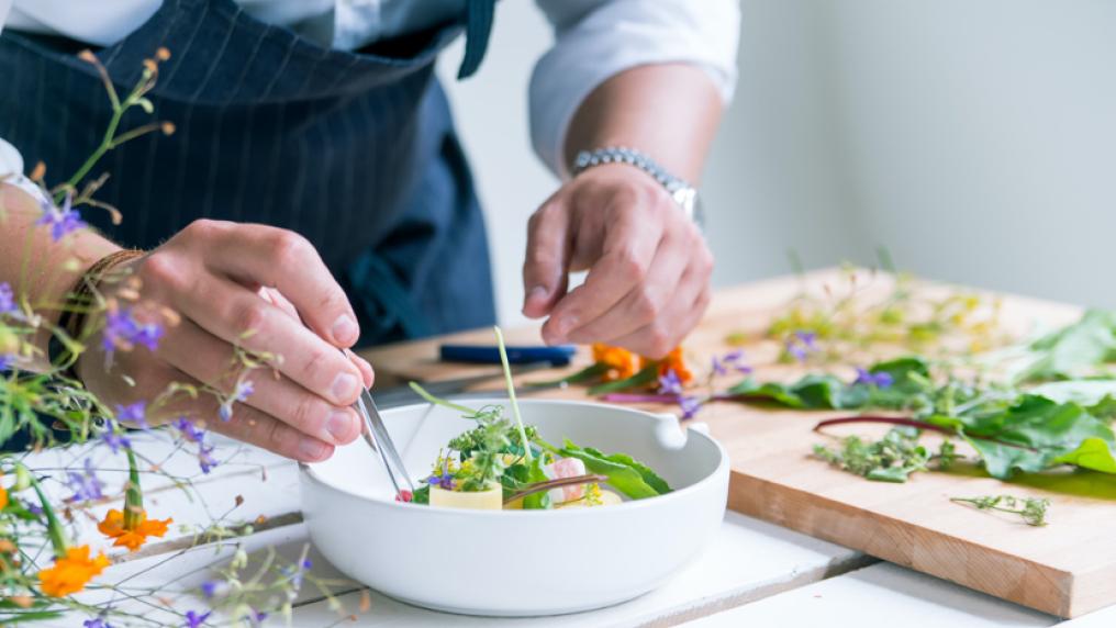 A chef decorates a beautiful dish with edible flowers