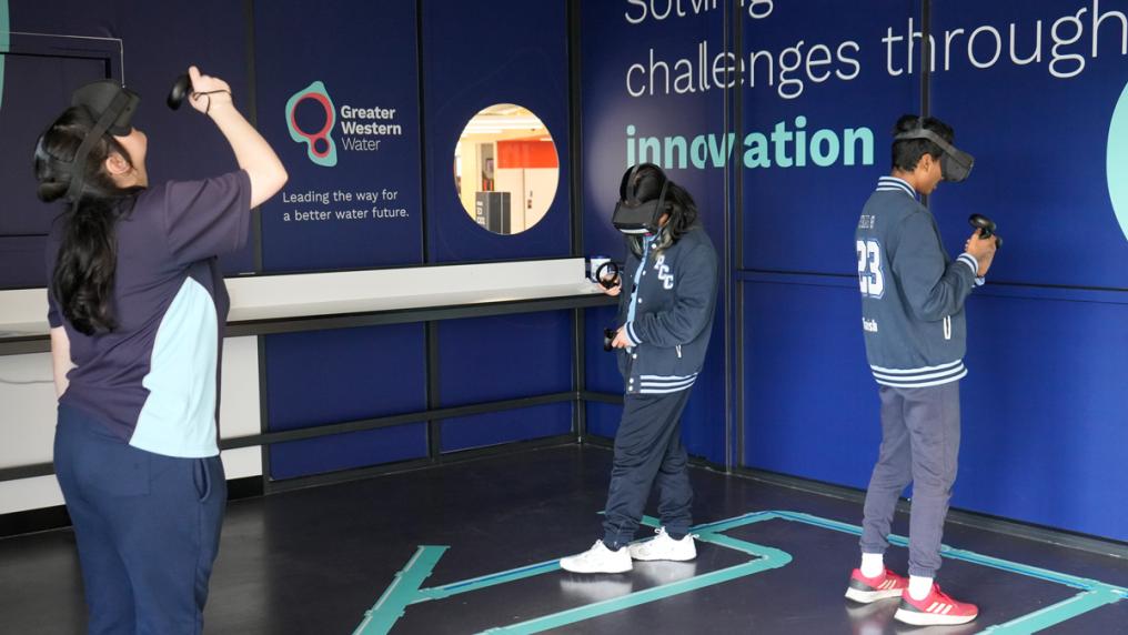 Three students walking around with VR headsets. Greater Western Water signage on the surrounding walls.