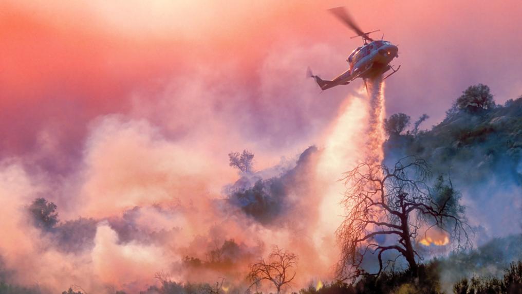 A helicopter dumping water over a burning landscape