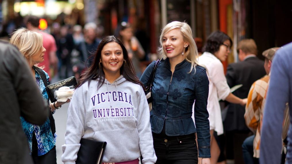 Two students standing in one of Melbourne's busy laneways. One of the students is wearing a Victoria University sweater.