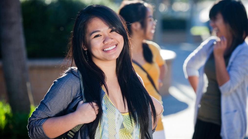 A young woman with a backpack smiles at the camera