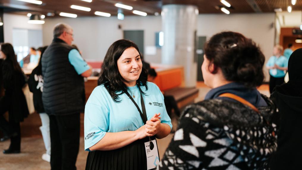 A smiling woman in a Victoria University t-shirt and lanyard helps with information