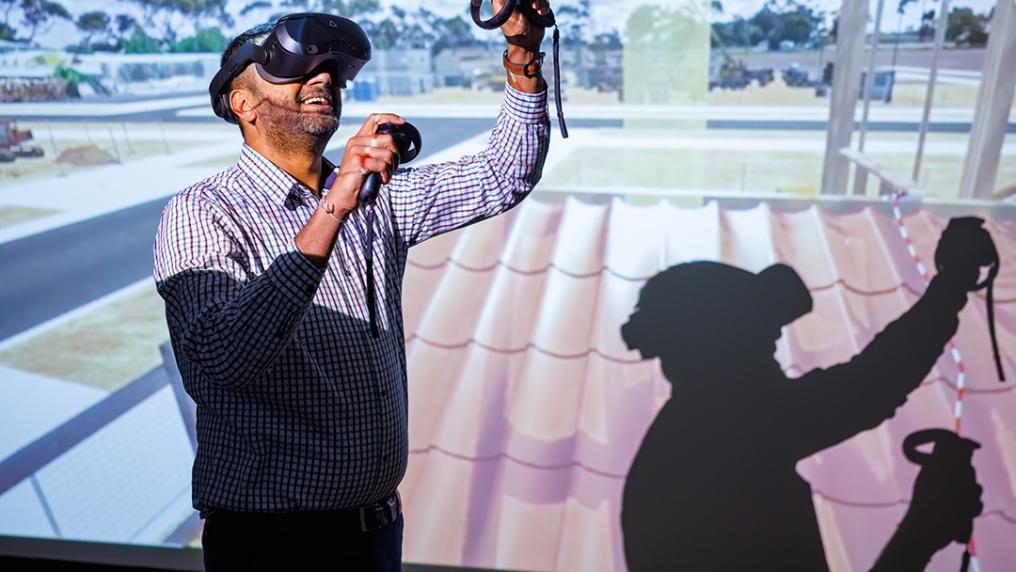 A man in a VR headset in front of a digital screen displaying a building