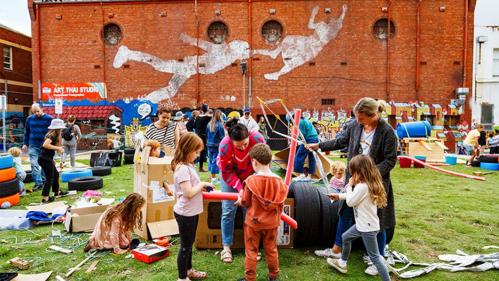 A group of kids and Early Childhood teachers gather on the grass in Footscray, engaged in tasks. Image credit: Gianna Rizzo.