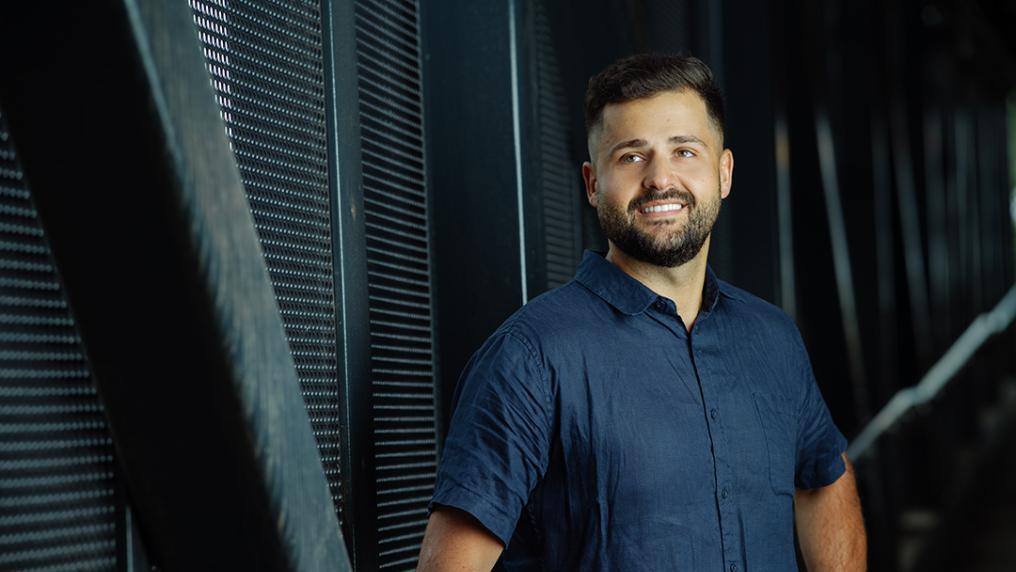 A man in professional dress poses in front of a modern steel wall