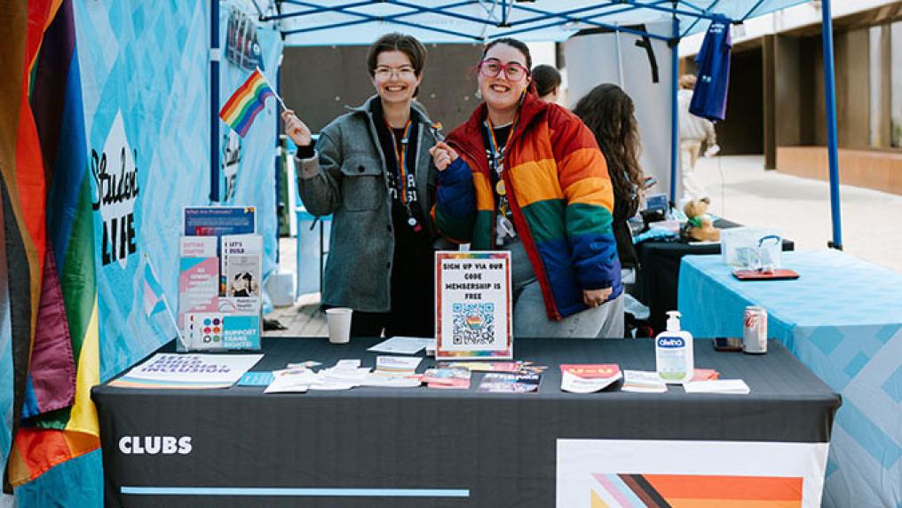 Two members of the VU Queer Collective stand at a stall. 