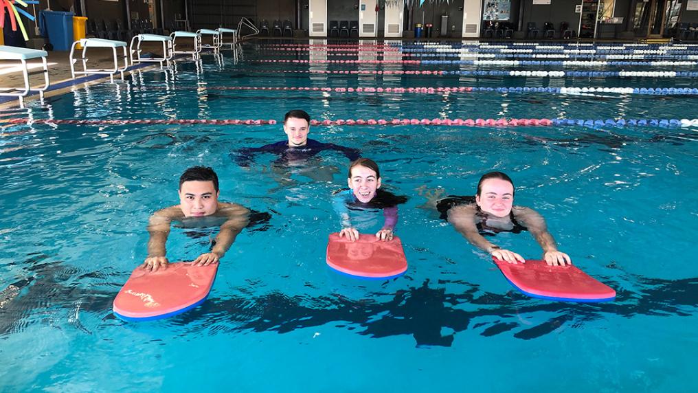 three young adult swimmers learning to swim using flutter boards
