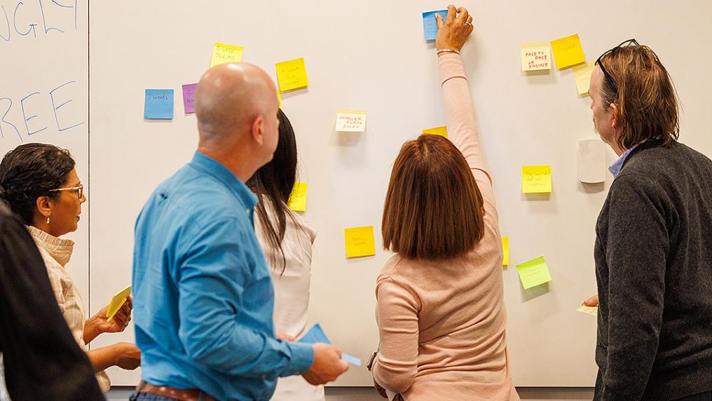 A group of professional men and women arrange sticky notes on a white board 