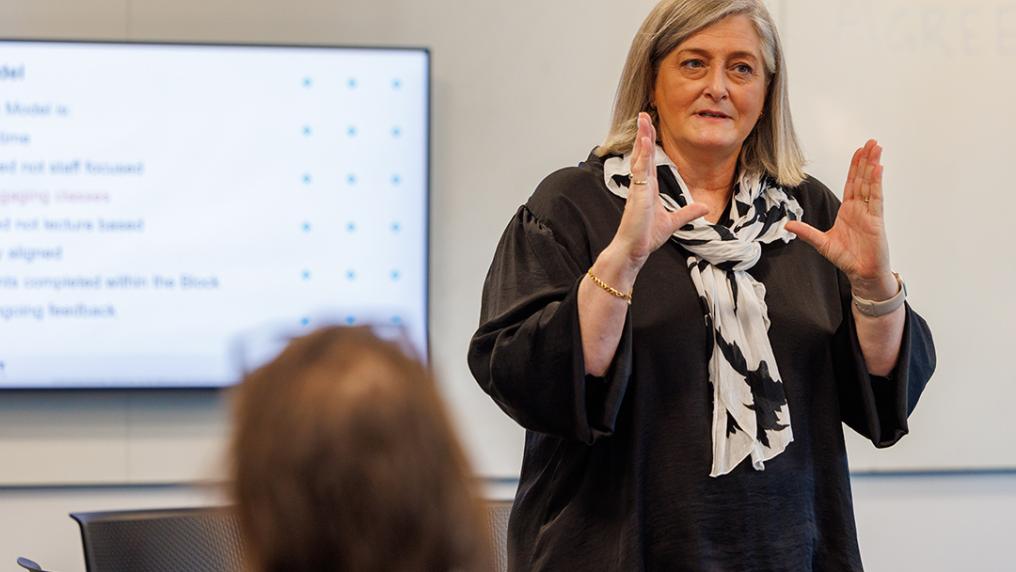 A woman gives a focused presentation in front of a digital screen