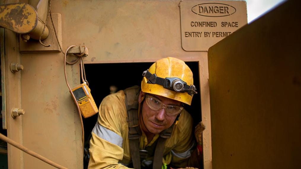 A construction working in a hard hat sits in a confined space.