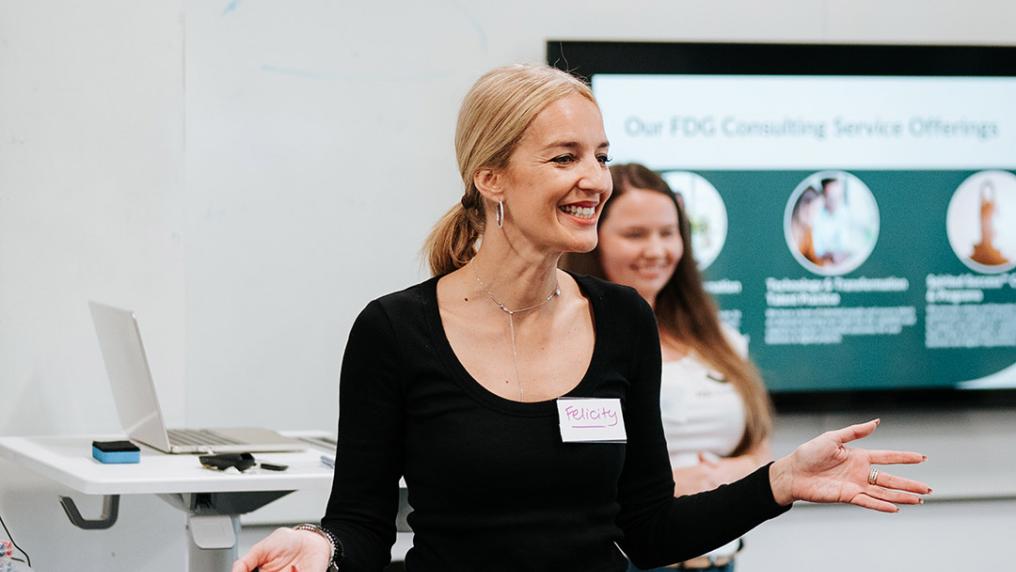 A woman smiles confidently in front of a digital presentation