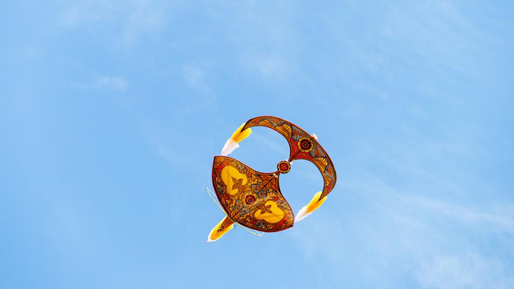A gold kite in the shape of a malaysian mask in a blue sky