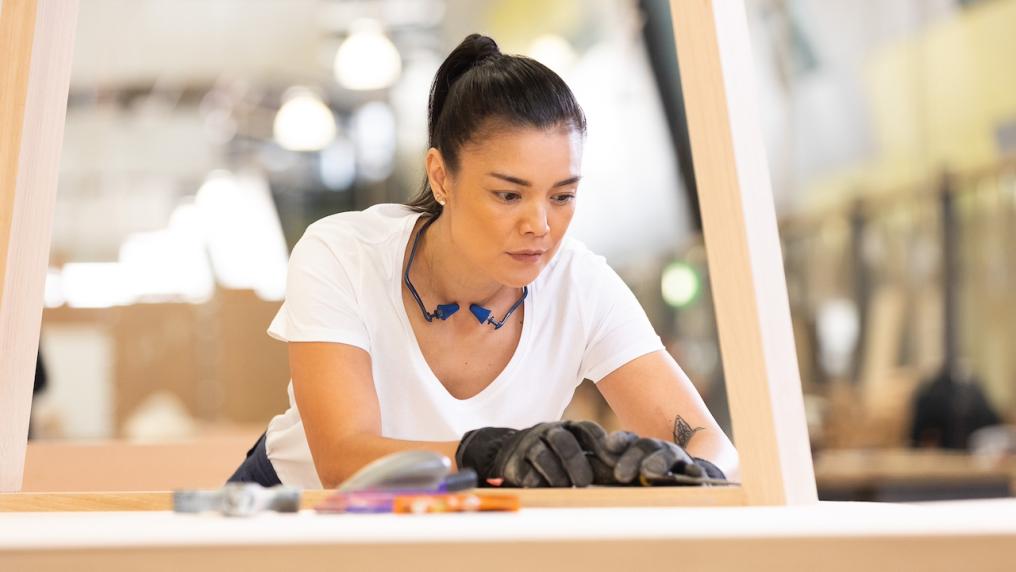 A TAFE student wearing a white shirt and protective gloves, focused intently on her work while woodworking.