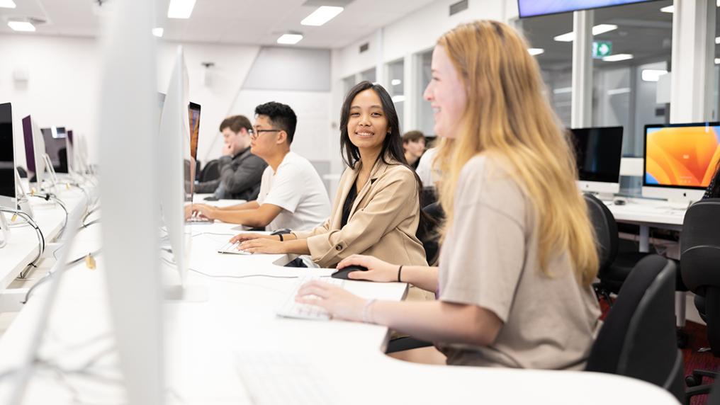 A group of young adults at computers in a modern, bright computer lab