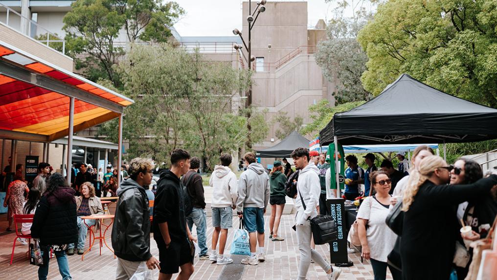 A large group of students walk among stalls on a campus courtyard