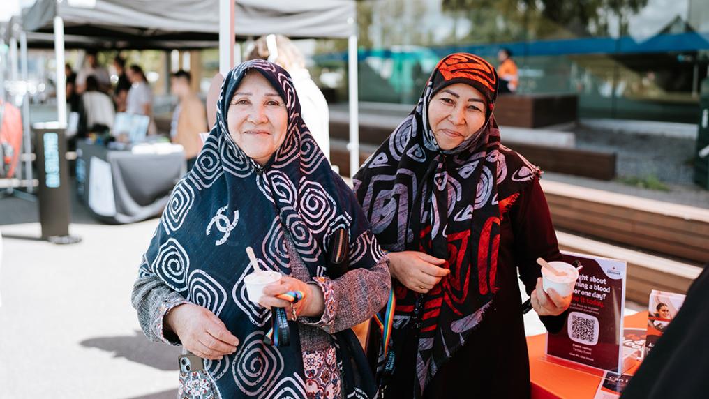 Two woman in hijabs in a sunny courtyard with stalls