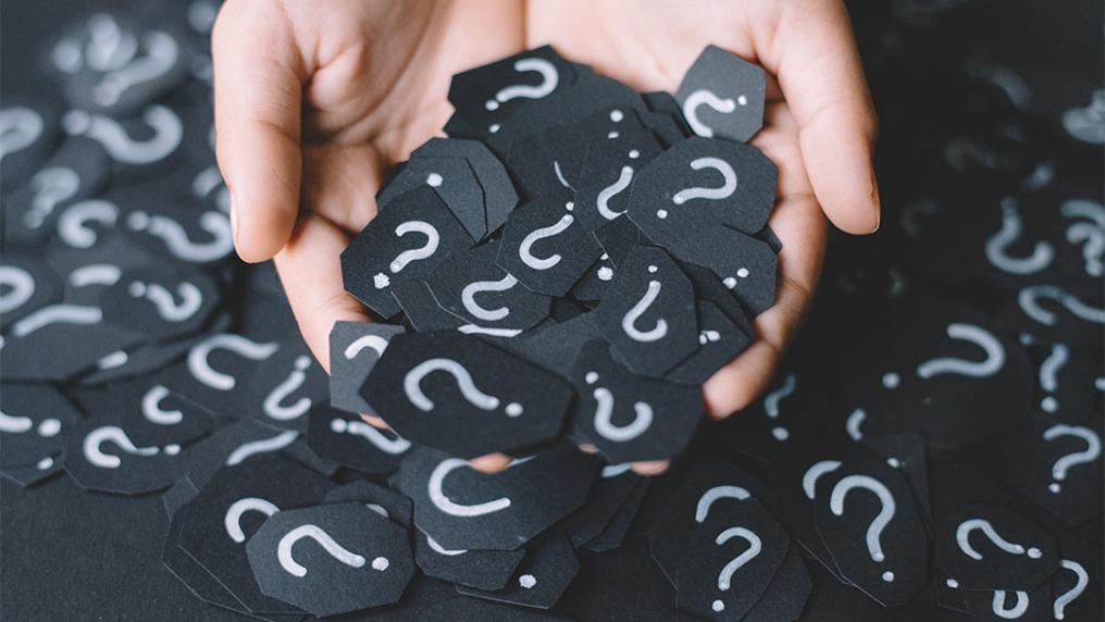 Hand holding small black cards with white question marks on it.