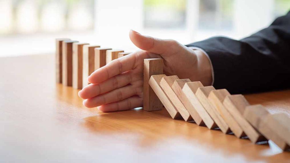 Hand blocking a row of wooden dominos from completely falling down.