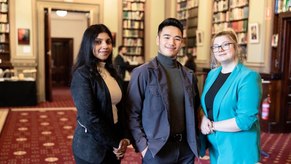 Three people stand in a room full of books.