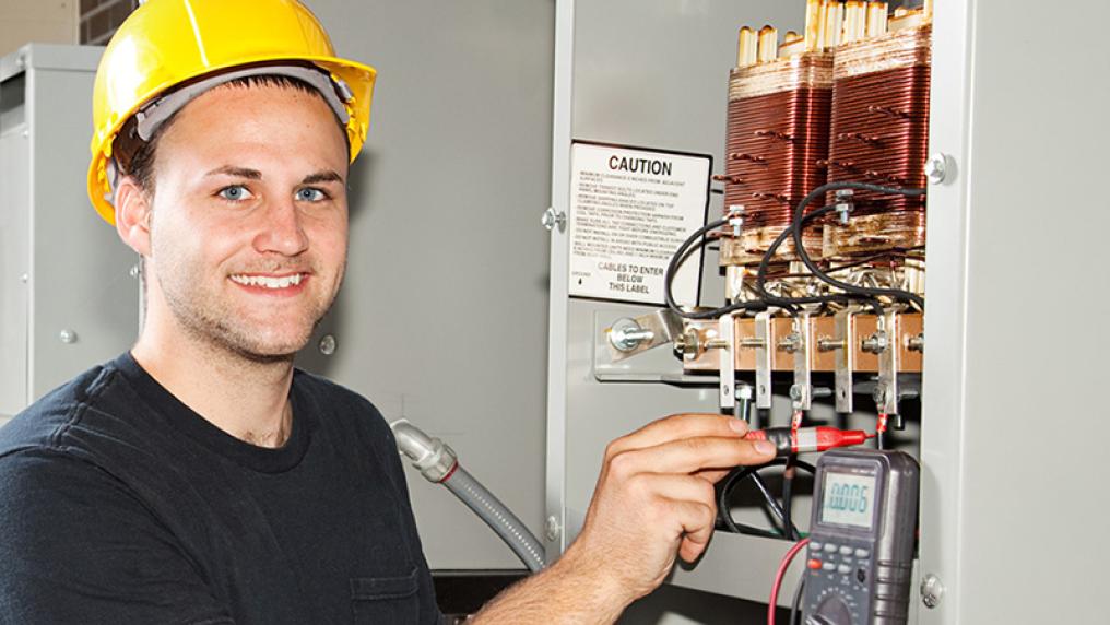 A young man in a hardhat works at an electrical circuit board