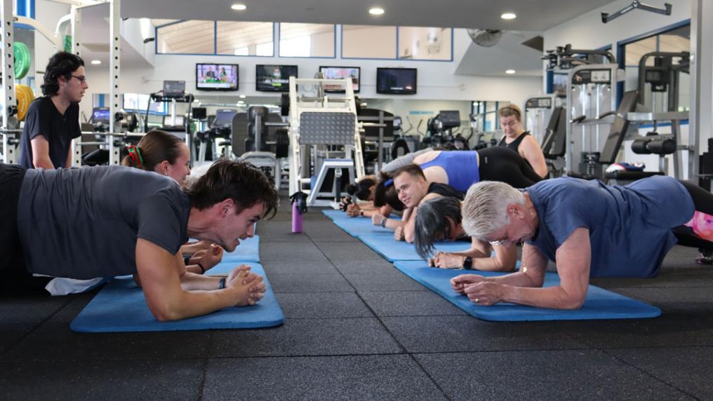 A group of people doing crunches on a yoga mat in a gym.
