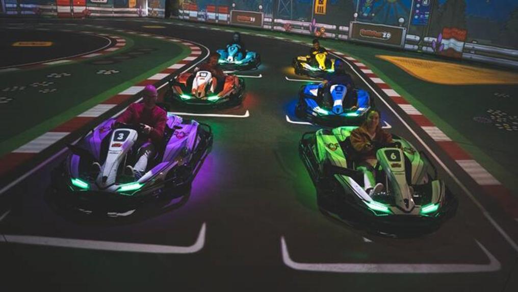 Rows of go-karts, lit up in neon colours, wait to take off in a darkened indoor racetrack