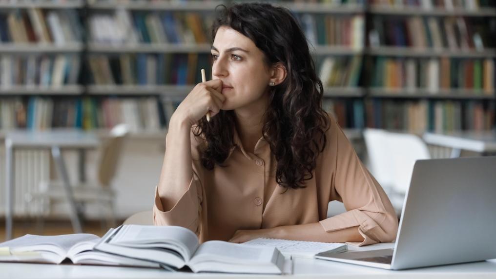 Female student looks pensive with laptop and books