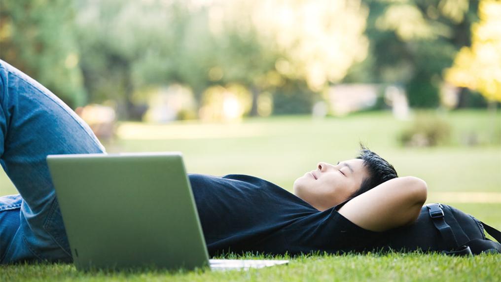A male university student lying down on the grass 