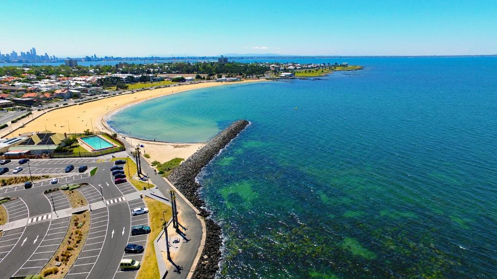 A suburb borders a white sand beach with a green-blue ocean bay