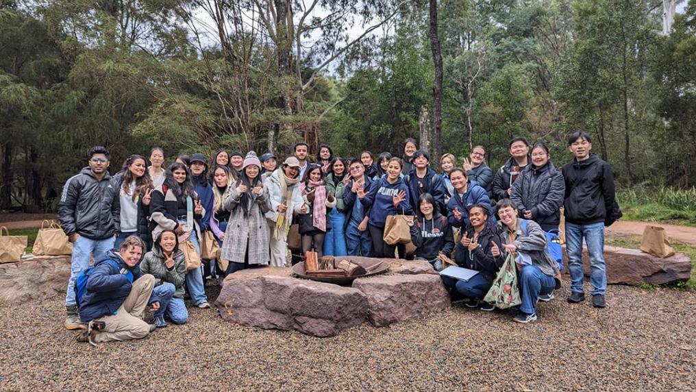 A group of university students smile and pose in front of eucalyptus trees
