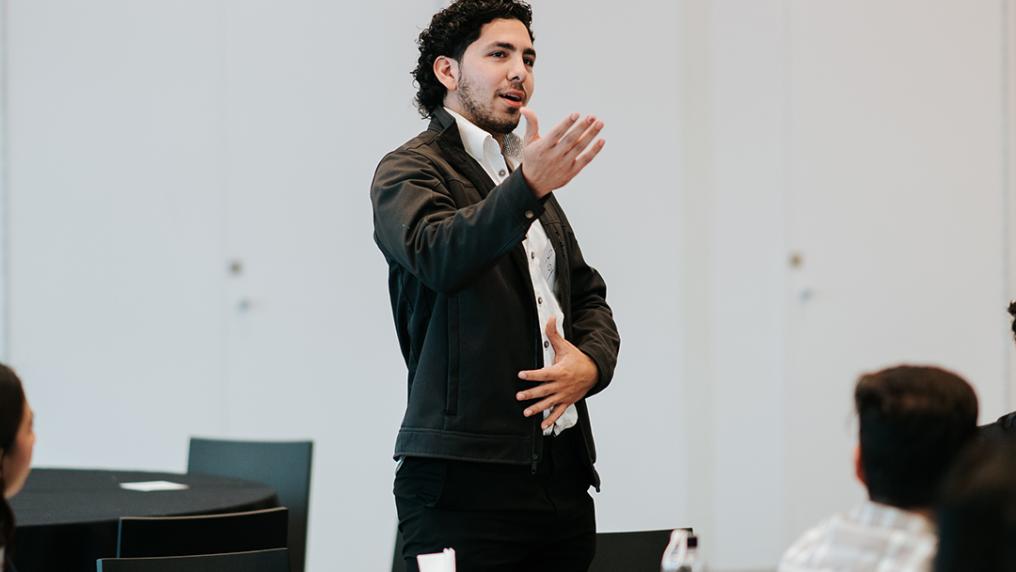 A young man in professional dress presents during a workshop