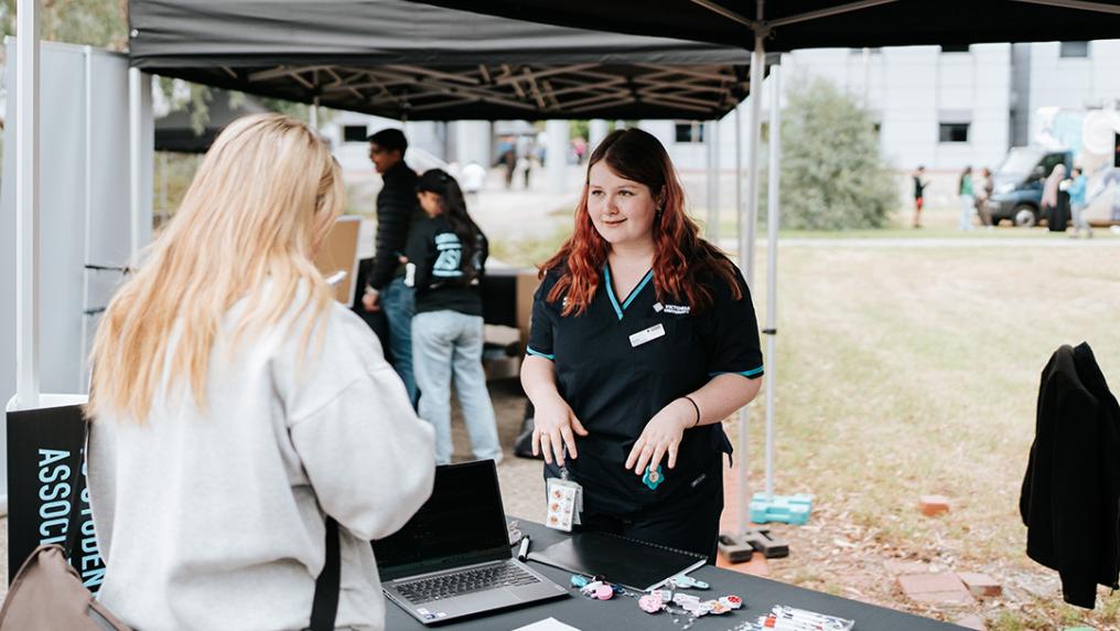 A young woman in a Victoria University polo shirt helps someone at an information stall