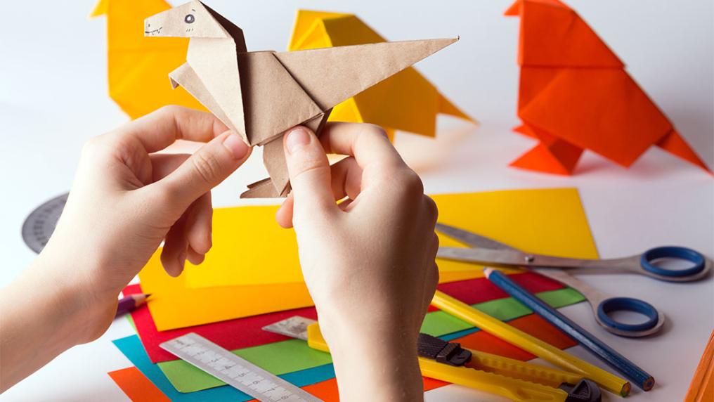 Hand holding an origami dinosaur with other crafting details in the background.
