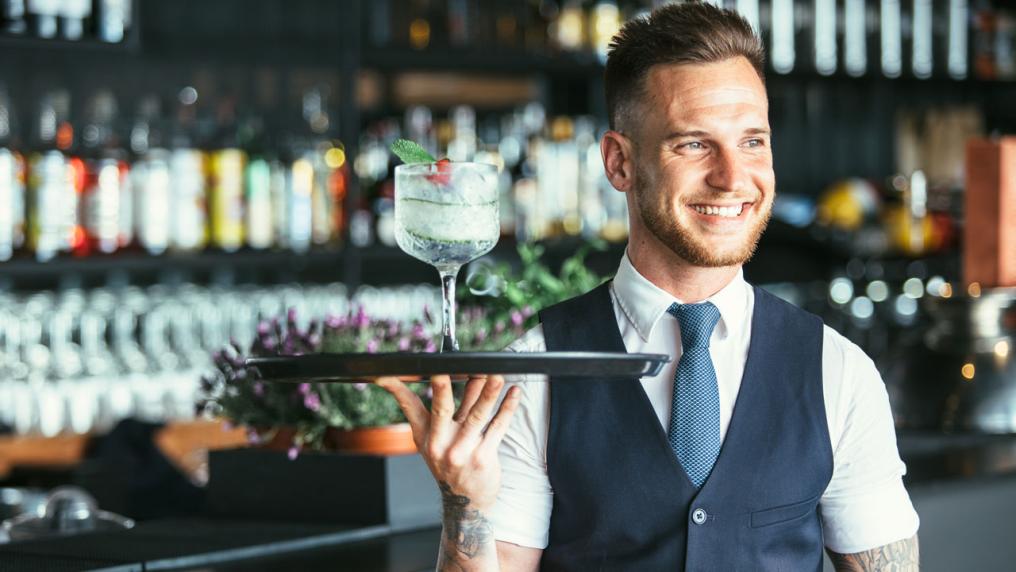 A bar employee holding a cocktail on a serving plate.