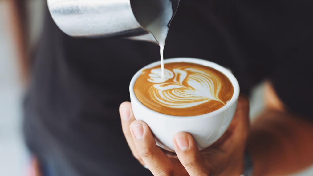 A person pouring steamed milk into a coffee cop, making latte art.