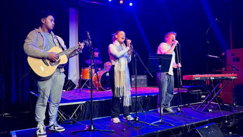 A group of young musicians perform on a indigo stage
