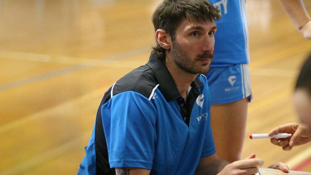 A young man in a VU blue sports uniform makes notes at a basketball court