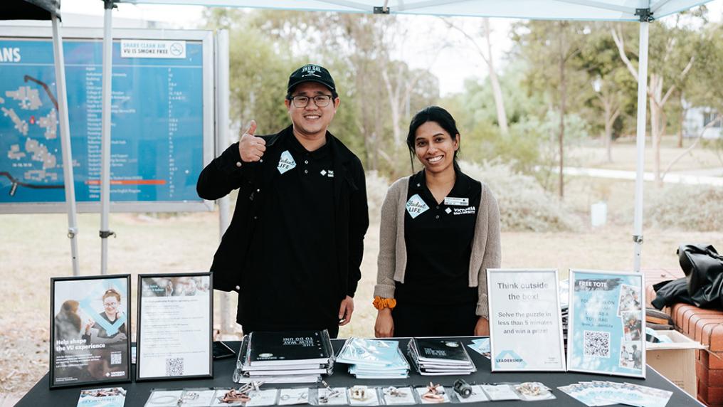 Two happy international students at an outdoor stand with information about Victoria University